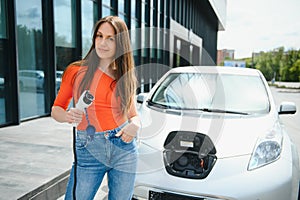 Charging car. Young woman in casual clothes with her electromobile outdoors at daytime