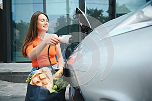 Charging car. Young woman in casual clothes with her electromobile outdoors at daytime