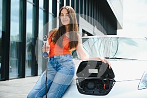 Charging car. Young woman in casual clothes with her electromobile outdoors at daytime