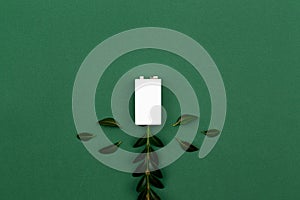 Charging Eco energy or green power illustration with a white battery and sprigs leaves on a green background with copy space for