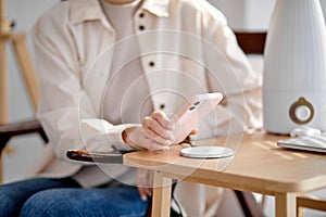 Charging mobile phone battery with wireless charging device on table, close-up hands
