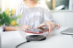Charging mobile phone battery with wireless charging device in the table. Smartphone charging on a charging pad