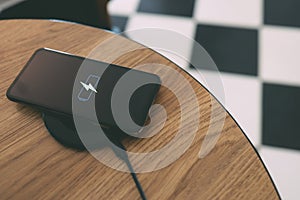 Charging mobile phone battery with wireless charging device in the table. Smartphone charging on a charging pad. Mobile phone near