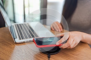 Charging mobile phone battery with wireless charging device in the table. Smartphone charging on a charging pad. Mobile phone near