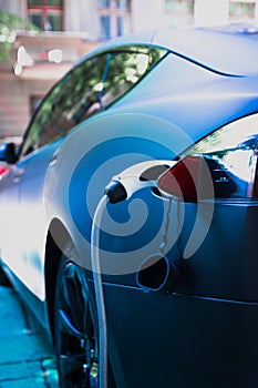 Charging modern electric car with cable plug inserted ir public parking lot