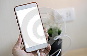 Charging a smartphone via a USB cable on woman hand. Close up of a white smartphone with a white blank screen