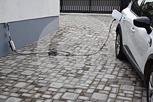 Charging white electric car from home power grid on backyard. Hybrid car Electric charger.