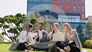 Charismatic black guy office manager and his team group of ladies working together at the fresh air on the grass in the