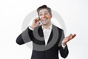 Charismatic businessman talking on smartphone and laughing, have lively phone call, standing happy in black suit against