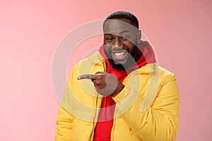 Charismatic carefree handsome black bearded guy in yellow jacket laughing friendly look camera chat pointing left show