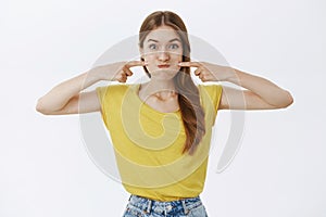 Charismatic funny and happy charming young female in yellow t-shirt pouting poking cheeks with index fingers and smiling