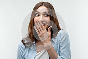 Charismatic girl with long chestnut hair covers her mouth with her hand. Human emotions, facial expression concept