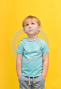 A charismatic handsome blond boy stands and looks upstairs on a yellow spring bright background with place for text