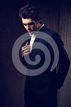 Charismatic handsome male model posing and looking down in fashion suit and white style shirt on dark shadow background. Closeup
