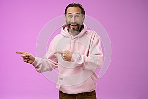 Charismatic happy good-looking mature 50s man wearing stylish hipster hoodie smiling excited pointing left index fingers