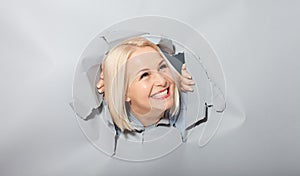 Charismatic joyful woman with blonde hairstyle, looking playfully, wears fashionable hoody, stands in torn paper hole, notices