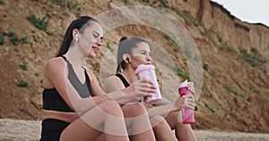 Charismatic young women have a conversation after the workout sitting down on the beach in front of the sea