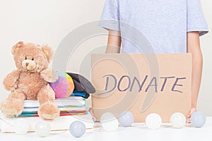 Charity, donation. Kid hands holding brown piece of cardboard with inscription Donate. Volunteer collect kid clothes