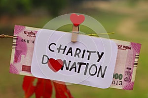 Charity donation phrase handwritten on paper with currency clipped to a branch of a tree