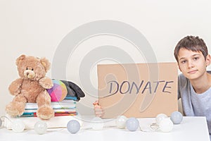 Charity, donation. Smiling kid holding brown piece of cardboard with inscription Donate. Volunteer collect kid clothes