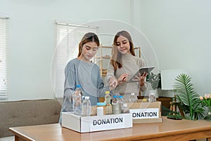 charity, donation and volunteering concept - Volunteer prepare foodstuff box containing food to donate and use tablet to