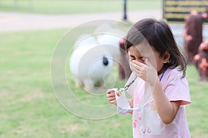 Charming 4 years old cute baby Asian girl, little preschooler sick child blowing nose with flu symptoms coughing outdoor.