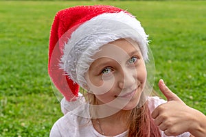 Charming 8 years old girl in santa claus hat raises a finger up and smiles. Christmas. New year concept. copy space