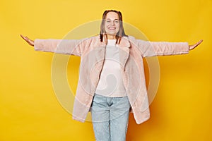 Charming adorable woman dressed pink fur coat isolated over yellow background spreading arms pretending flying looking smiling at