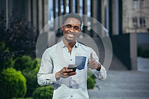 Charming african american man happy looking at camera, holding mobile phone in hands smiling and happy