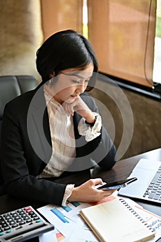 Charming Asian businesswoman checking messages on her smartphone at her desk