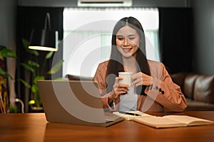 Charming asian businesswoman drinking coffee and reading email on her laptop computer
