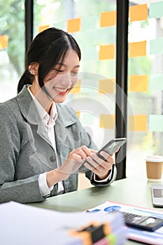 Charming Asian businesswoman or female office worker using her smartphone at her desk