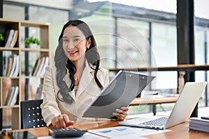 A charming Asian businesswoman sits at her desk and looks at the camera