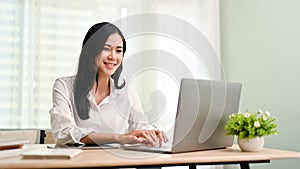 Charming Asian businesswoman working in her office, typing on keyboard, using laptop