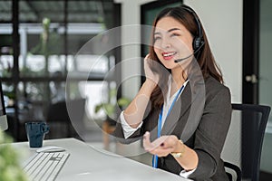 A charming Asian female call centre operator with a headset is working at her desk