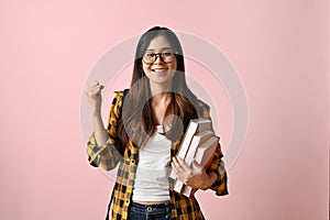 Charming Asian female college student Yes gesture, holding schoolbooks, pink isolated background