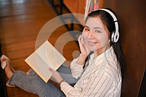 Charming Asian female listening to music through her headphones, holding an opened book