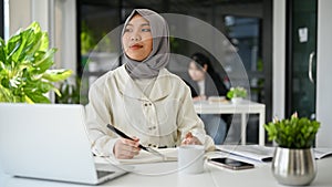 Charming Asian Muslim female office worker daydreaming, looking out the window