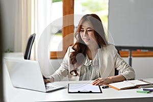 Charming asian woman entrepreneur using laptop computer and working with financial document