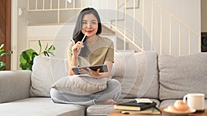 Charming asian woman using digital tablet on couch in cozy living room, enjoying leisure weekend time alone at home