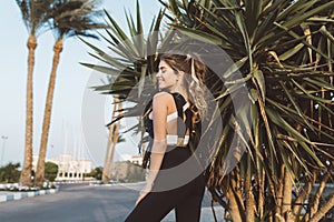 Charming attractive young woman from back at training in sunny morning on street with palm trees in tropical city photo