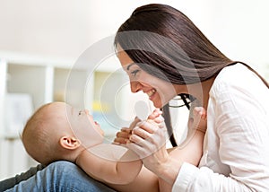 Charming baby boy looking at mommy and smiling while lying on his mother`s knees. Mom is looking at her child son