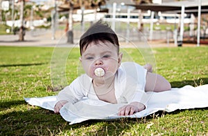 Charming baby girl with dummy lying on a green grass