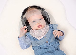 Charming baby girl is lying on the floor and hearing music wearing in headphones