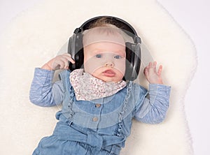 Charming baby girl is lying on the floor and hearing music wearing in headphones