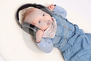 Charming baby girl is lying on the floor and hearing music wearing in headphones