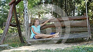 Charming barefoot girl smiling at the camera. Pleasant rest on a wide swing in the park