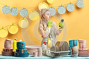 Charming beautiful girl in gloves holding smart phone while doing dishes
