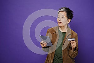 Charming beautiful mature woman hold credit card and tablet pc in hand dreaming about online bank credit. E-commerce