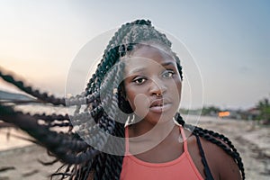 Charming beautiful young african american woman girl with black pigtails with piercings on her face on the beach at sunset